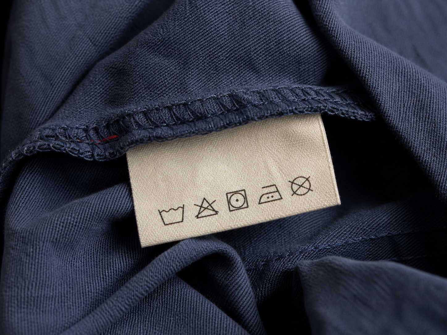 Laundry symbols on a cream care label sewn into navy cotton